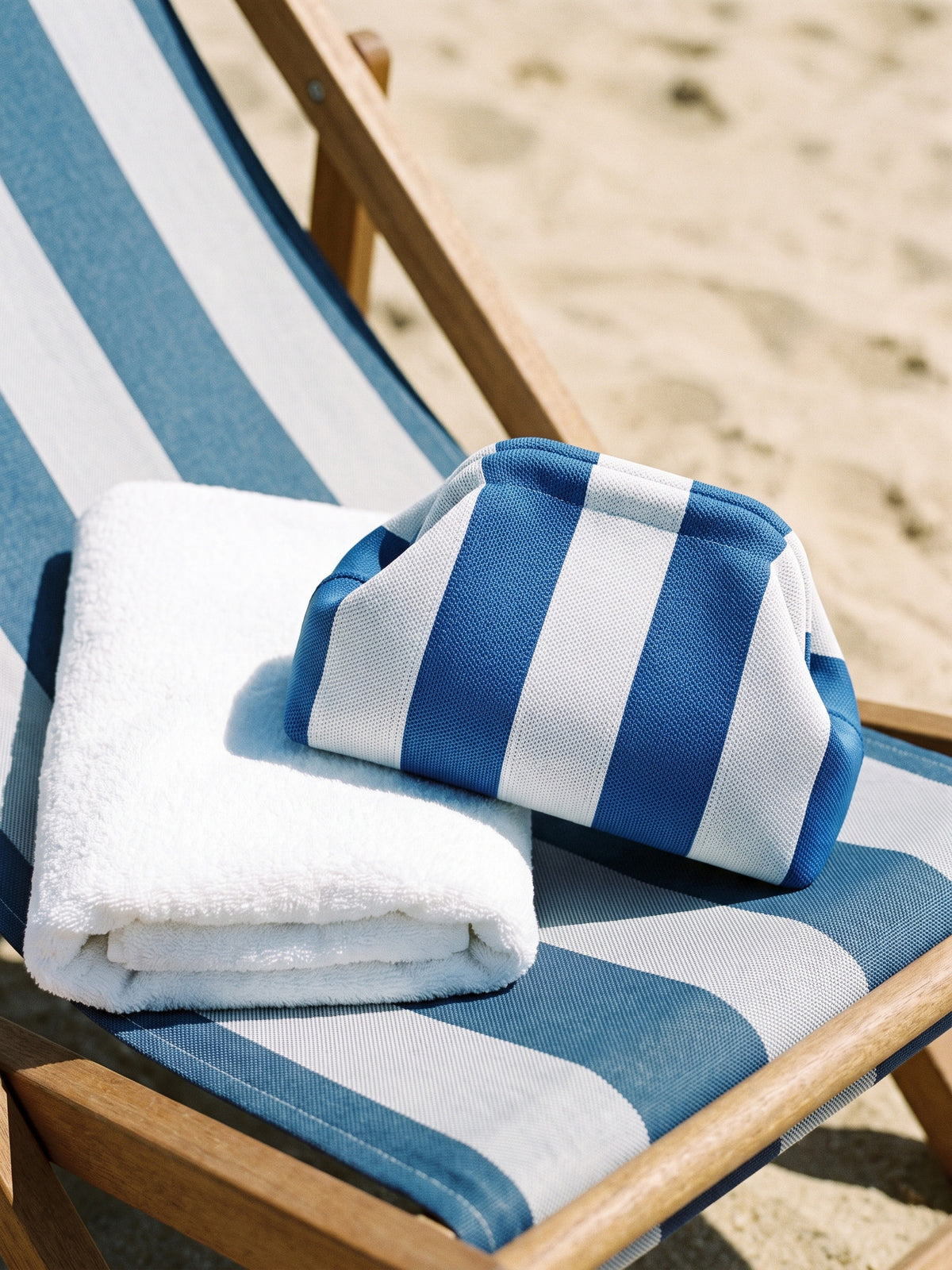 Cobalt & White Stripe Cloud Pouch — sits on a striped deckchair cushion beside a folded white towel of similar width