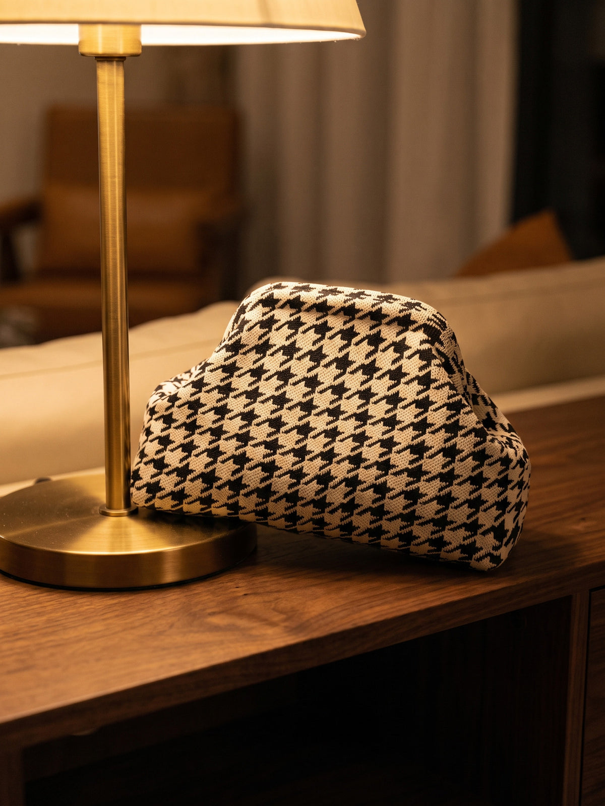 Monochrome Houndstooth Cloud Pouch — rests on a dark walnut console beside a slim brass lamp base