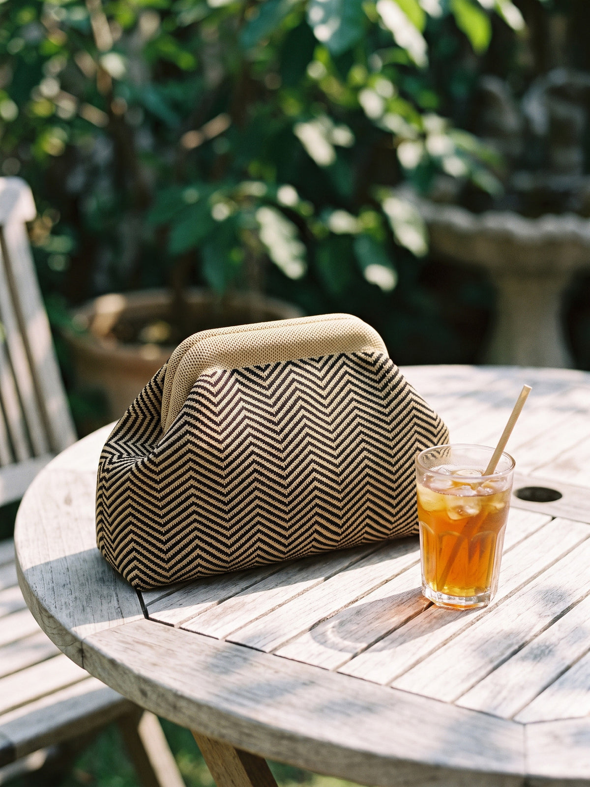 Olive Chevron Cloud Pouch — sits on a pale wooden garden table beside a small glass of iced tea that reaches most of the pouch's height