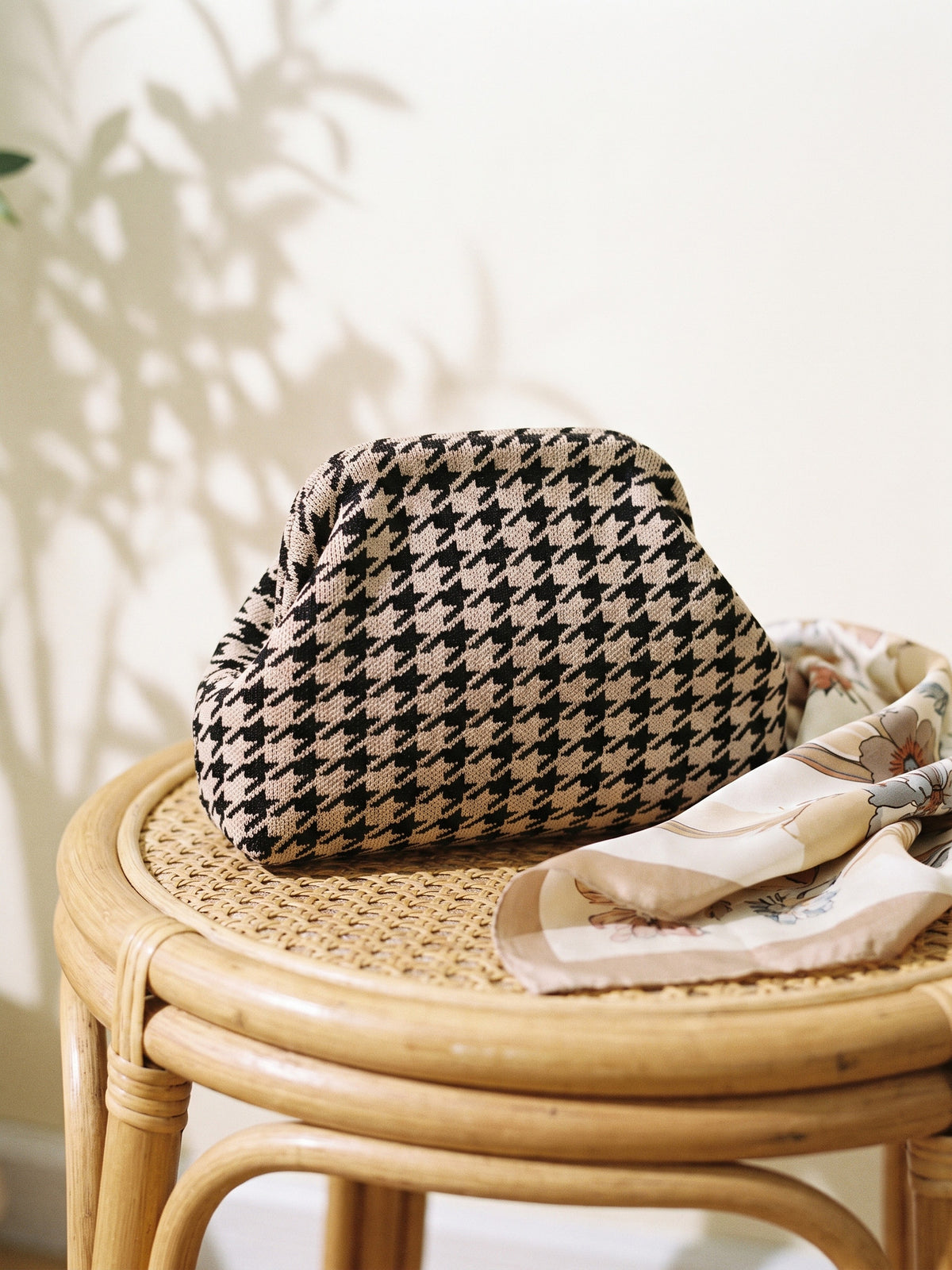 Cocoa Houndstooth Cloud Pouch — sits on a rattan stool beside a folded silk scarf