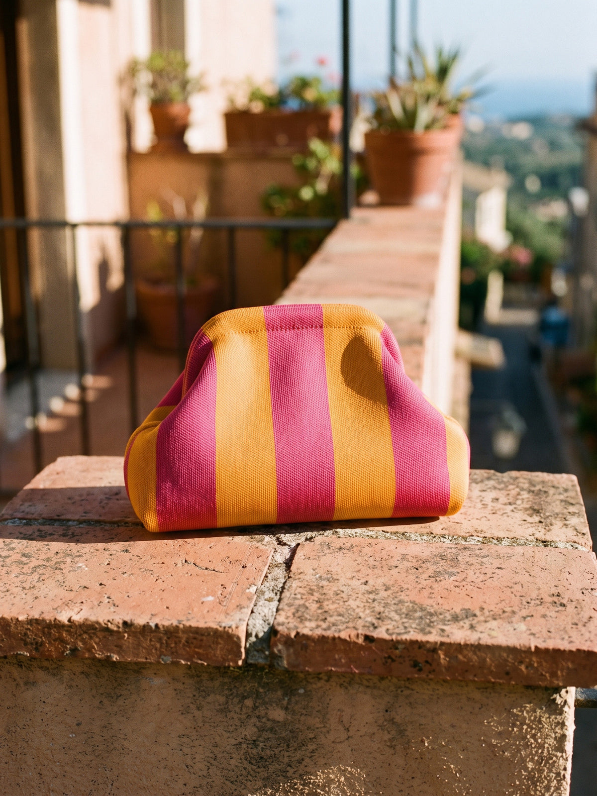 Marigold & Fuchsia Stripe Cloud Pouch — sits on a sunlit balcony ledge of terracotta tiles, spanning about two tiles