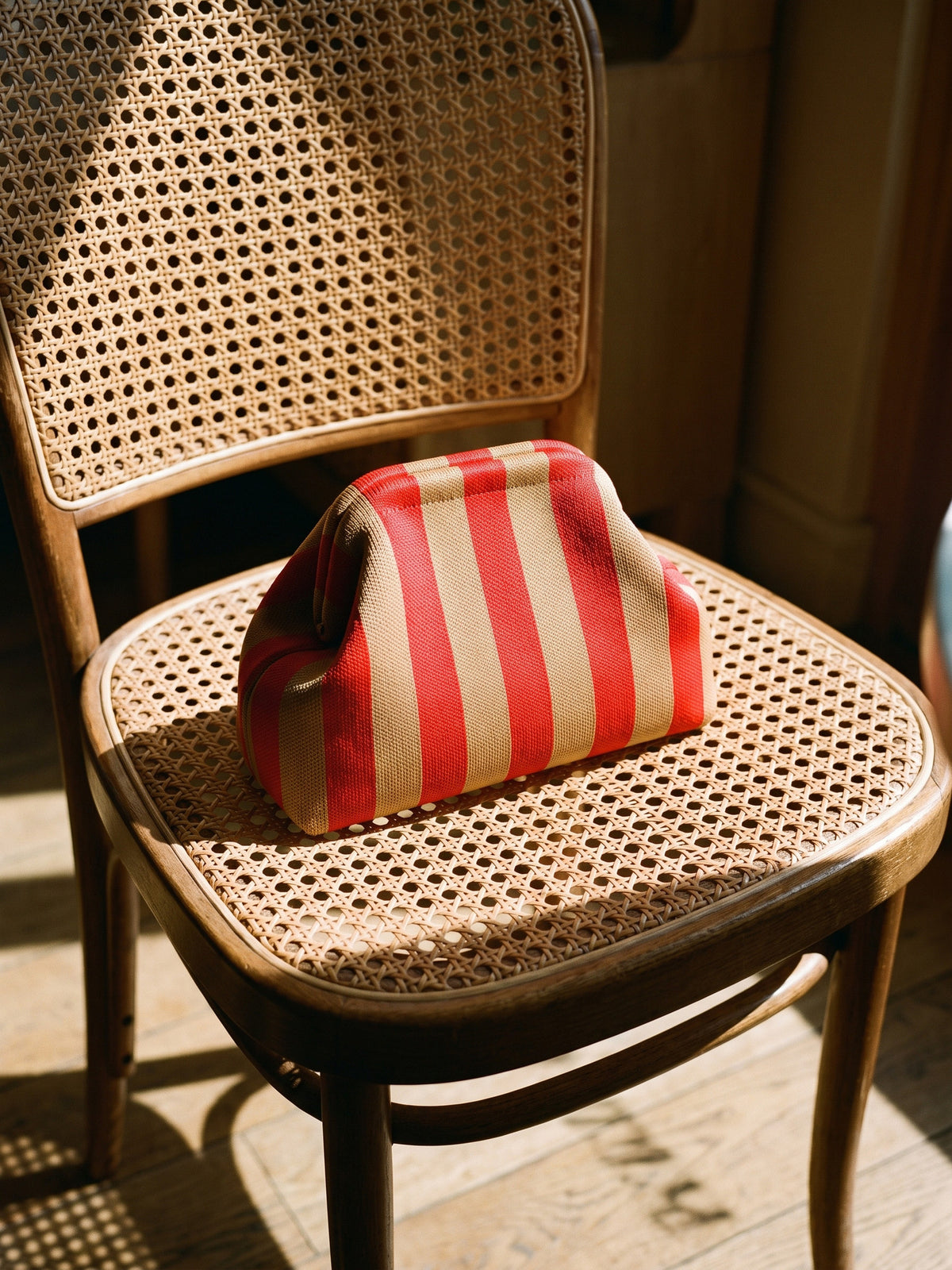 Poppy & Tan Pinstripe Cloud Pouch — rests on a cane cafe chair seat, covering roughly half the seat
