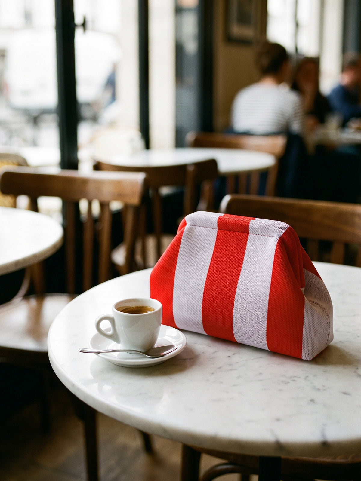 Red & White Stripe Cloud Pouch — sits on a small round marble cafe table beside a 6 cm espresso cup and saucer