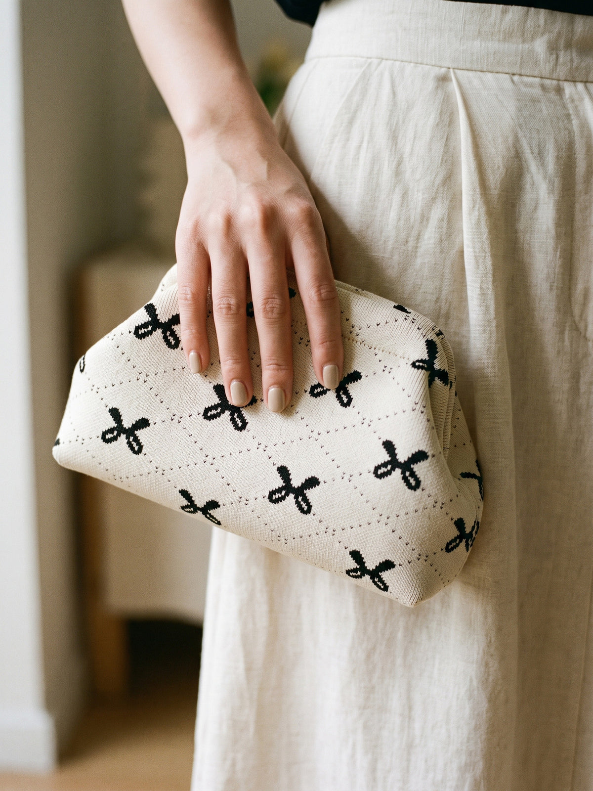 Cream Bow Cloud Pouch — held in one hand with a neutral manicure against a cream linen skirt at hip height