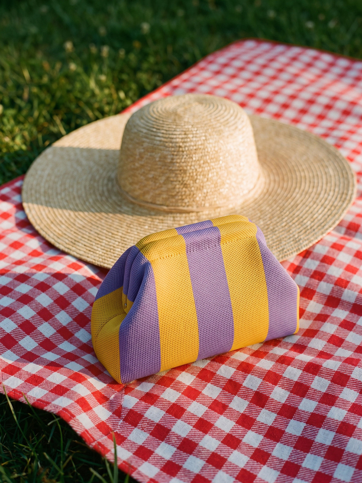 Marigold & Lilac Stripe Cloud Pouch — rests on a picnic blanket beside a straw sun hat that is clearly wider than the pouch