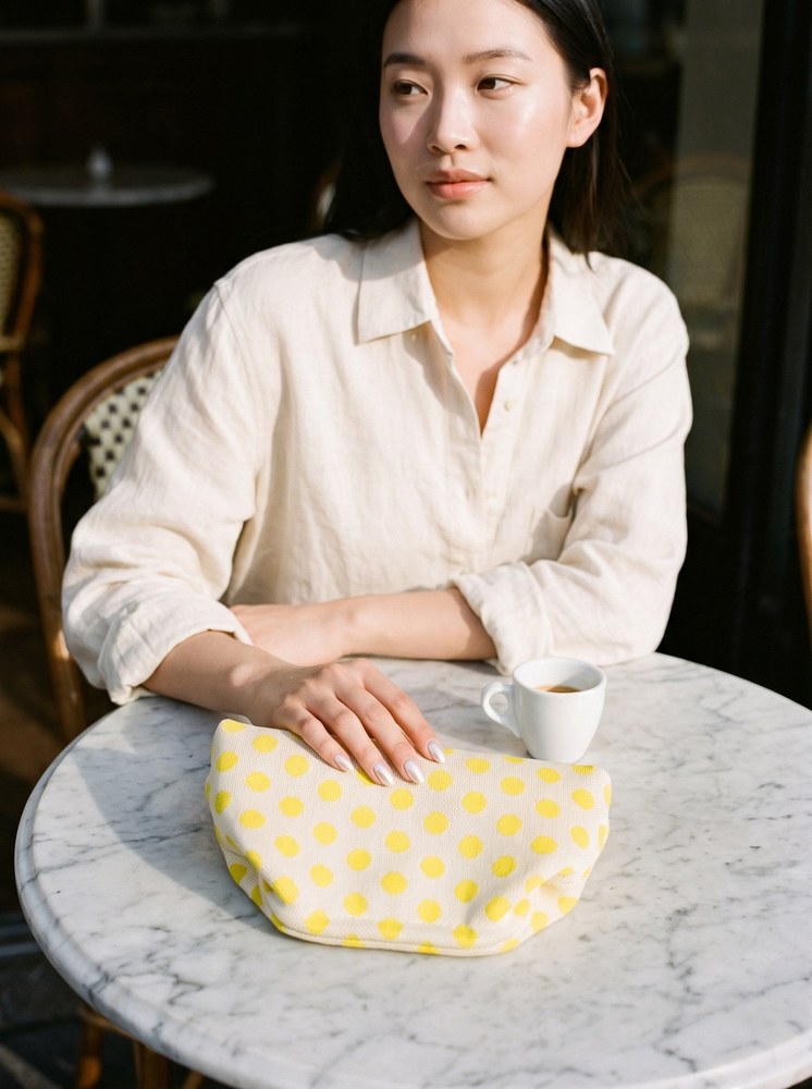 A woman at a marble cafe table with a lemon polka dot Etta Rowe cloud pouch beside her espresso