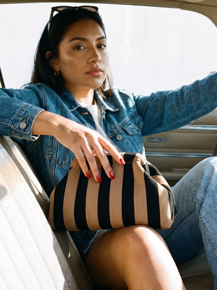 A woman in a denim jacket in a car with a camel and black striped Etta Rowe cloud pouch on her lap